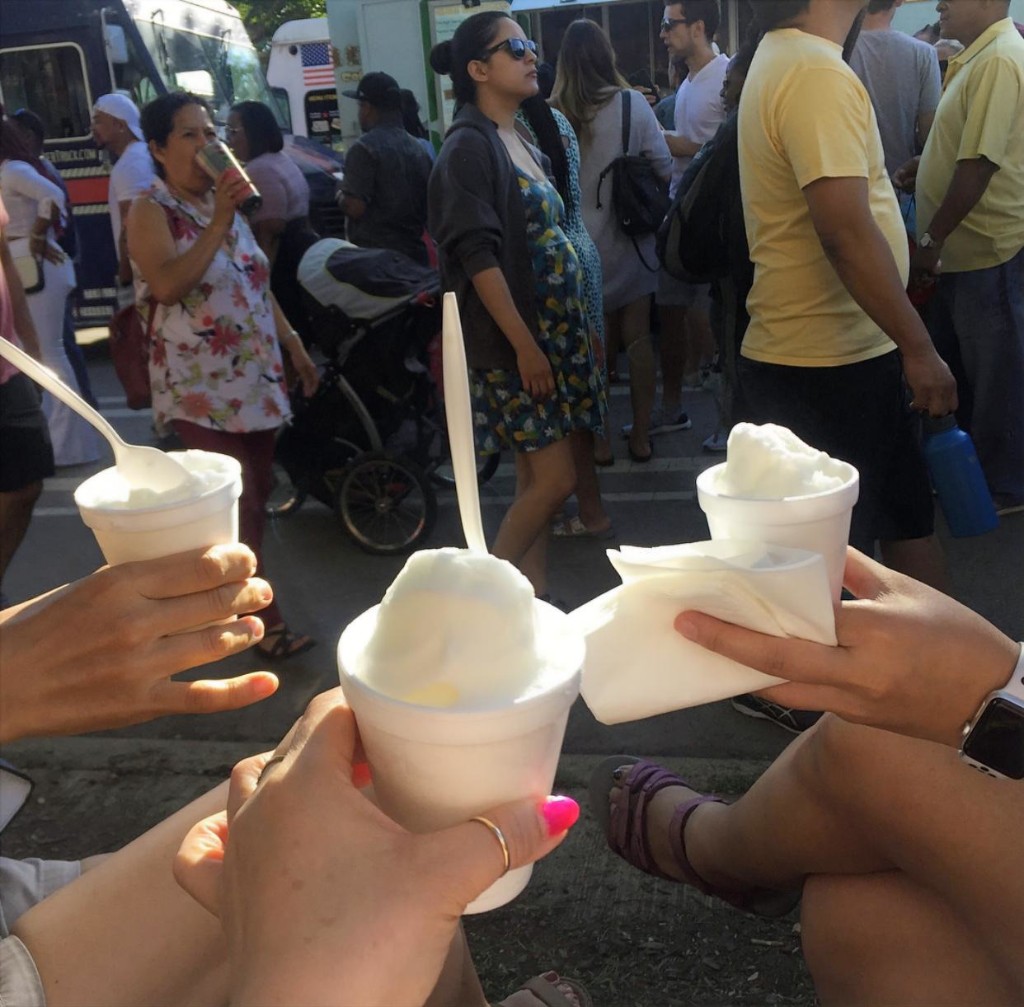 Two friends picnicking on the grass surrounded by festival guests in the park