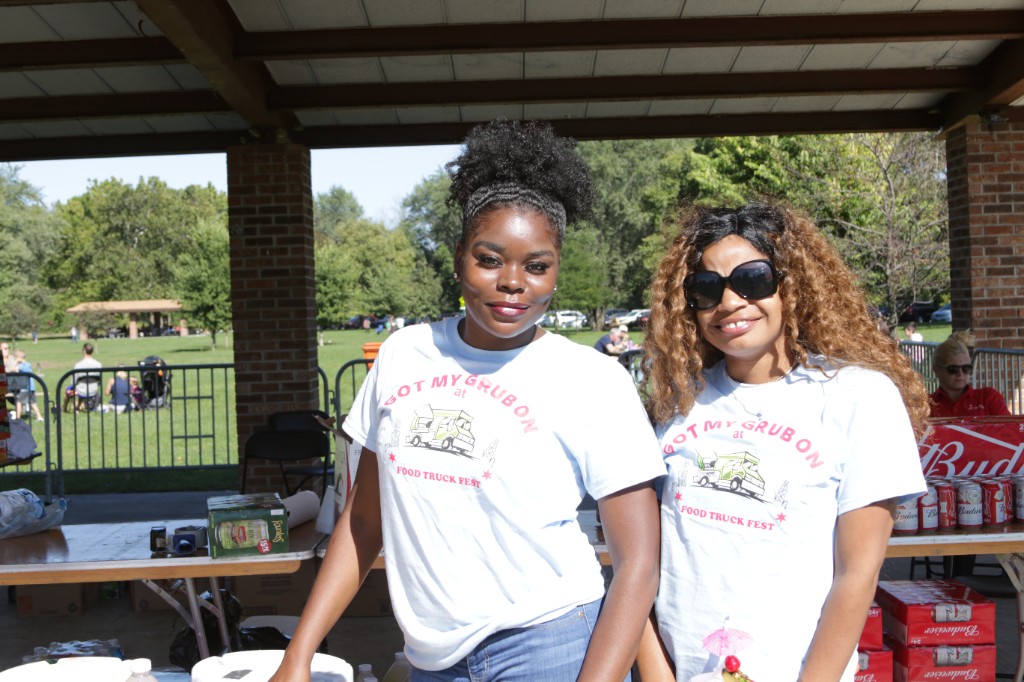 Two guests in Chicago Food Truck Fest shirts under a pavilion at Labagh Woods with the park lawn behind them.