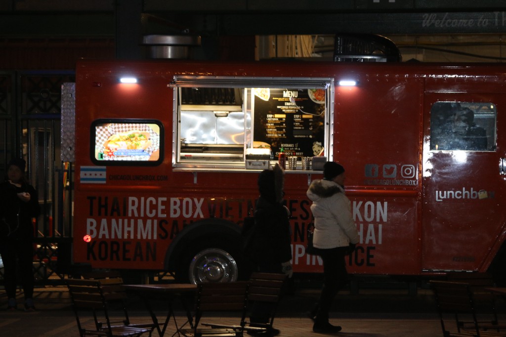 Food truck worker serving guests in winter coats at a brightly lit service window at night