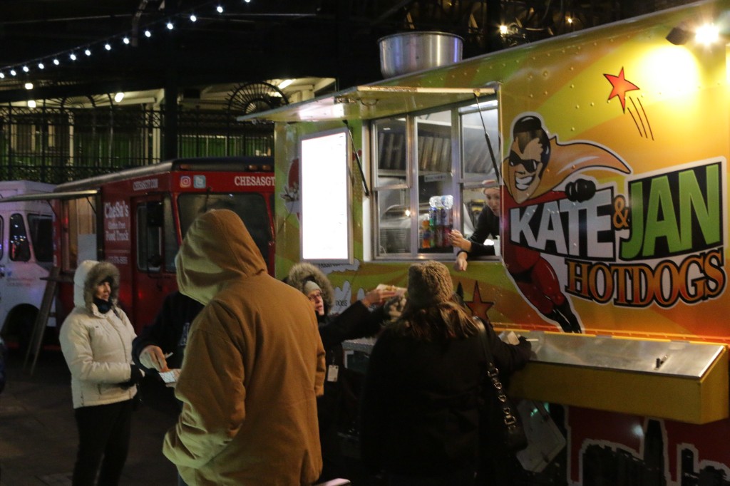Full band with plaid-shirt singer under pink and purple lights on an outdoor stage at Gallagher Way