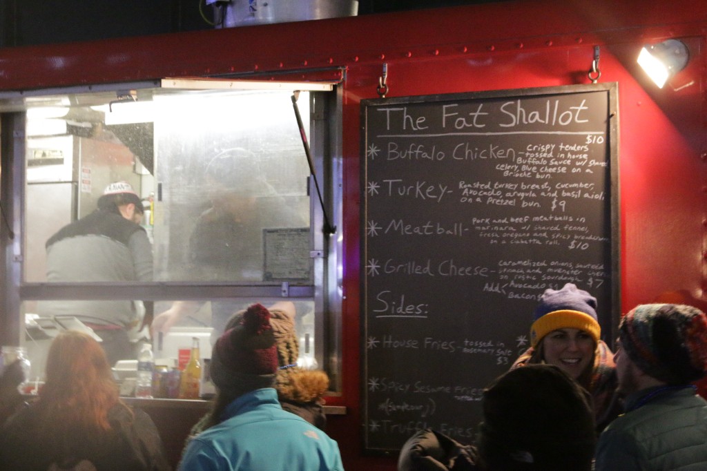 Guests in coats walking past food trucks and small bistro tables on the plaza