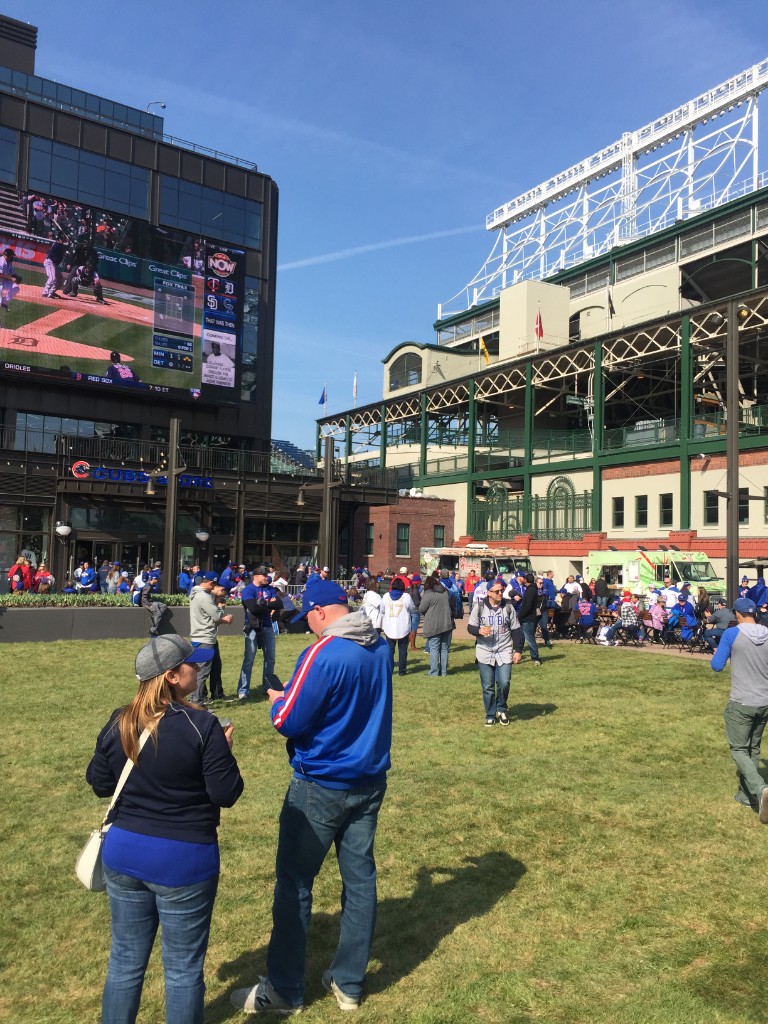 Gallagher Way lawn with fans, outdoor video screen, and Wrigley Field on a home game day