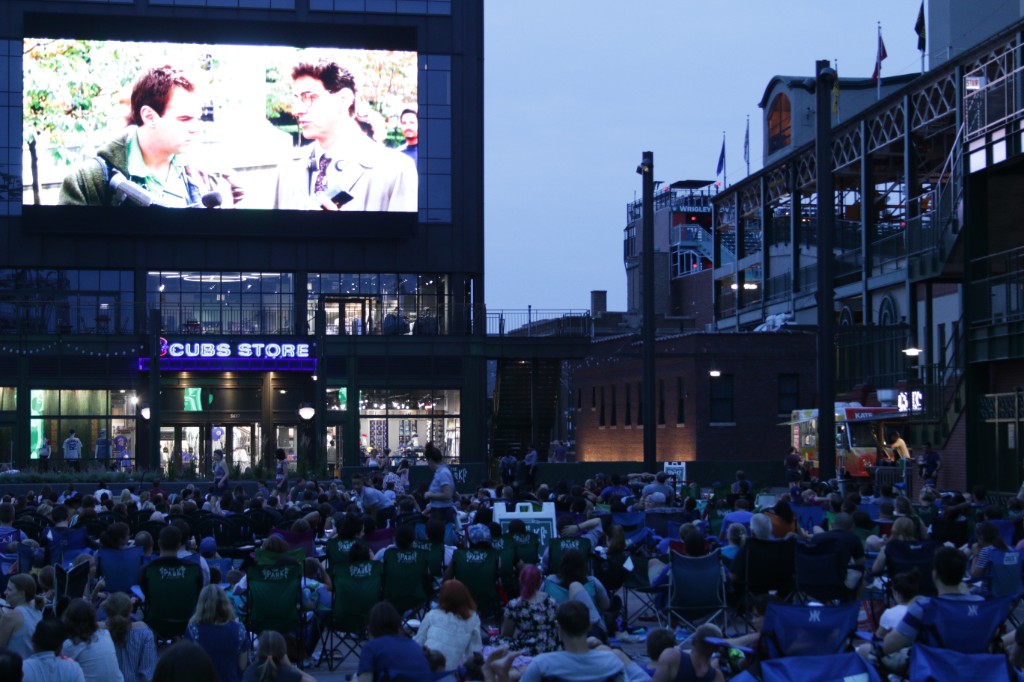 Twilight crowd on blankets and chairs with the outdoor screen and Wrigley Field in the background