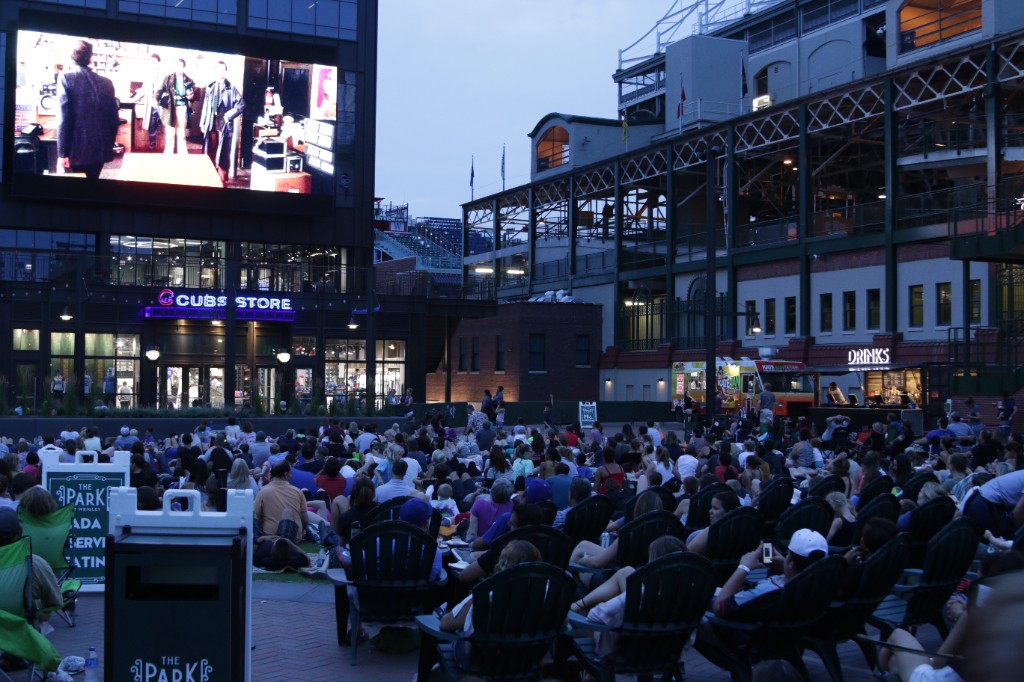 Guests on the turf facing the bright screen with concessions and stadium lights at dusk
