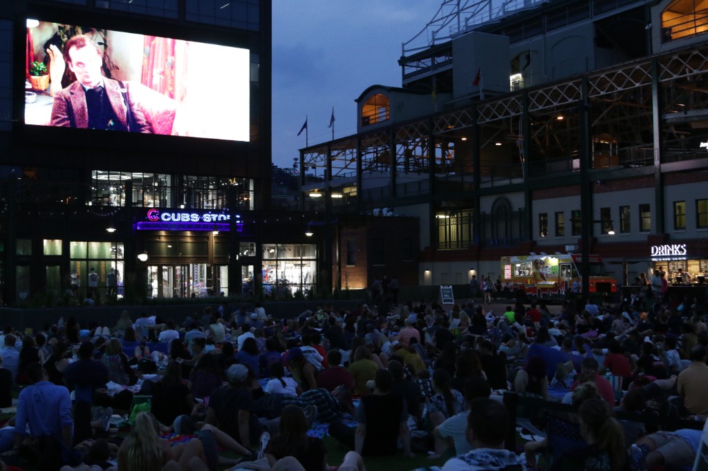 Wide view of the lawn audience, outdoor screen, and Cubs Store during an evening screening